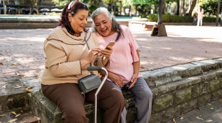 Two old women sitting at the park and using mobile phone