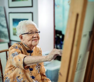 Asian chinese smiling senior women painting on canvas at her house waist up of active mature senior women painting on canvas with easel